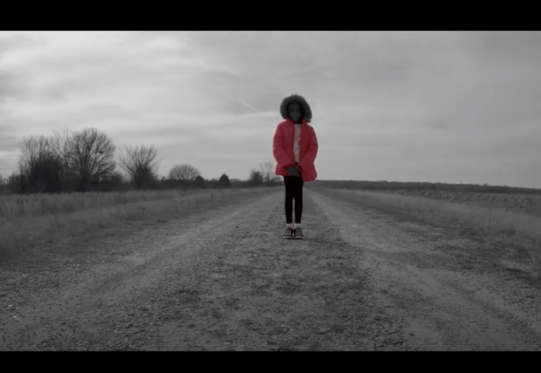 A African-American girl standing in the middle of a dirt road